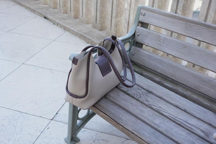 Bolso descansando en un banco de madera en un entorno urbano.