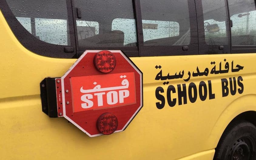 Un autobús escolar vacío con una señal de advertencia de parada roja estacionado al lado.
