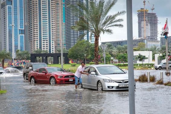 Personas empujando autos fuera del agua en calles inundadas de Dubái.