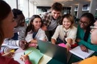 Un grupo alegre de estudiantes universitarios sentados en una mesa mirando un cuaderno.