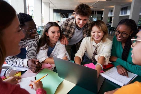 Un grupo alegre de estudiantes universitarios sentados en una mesa mirando un cuaderno.