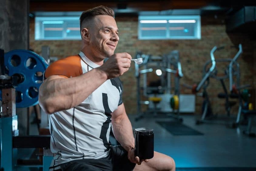 Culturista musculoso con un cuerpo perfecto sosteniendo proteína en el gimnasio.