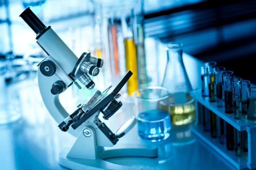 Microscopio sobre una mesa con tubos químicos y cristalería.