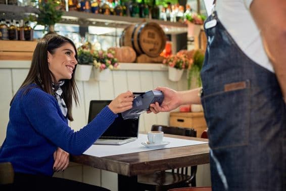 Mujer castaña sentada en una cafetería, pagando con tarjeta de crédito.