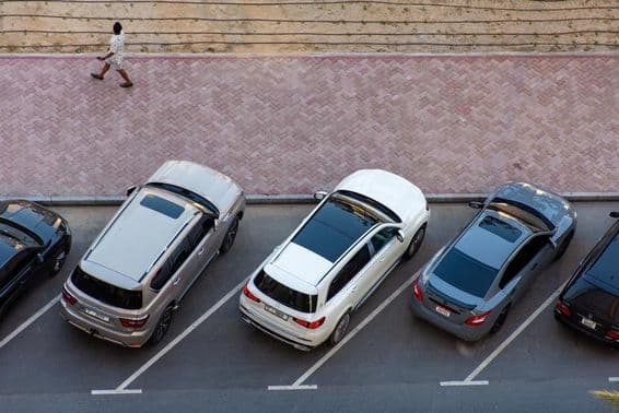 Vista aérea de autos estacionados en Dubai y un hombre caminando en una acera pavimentada.