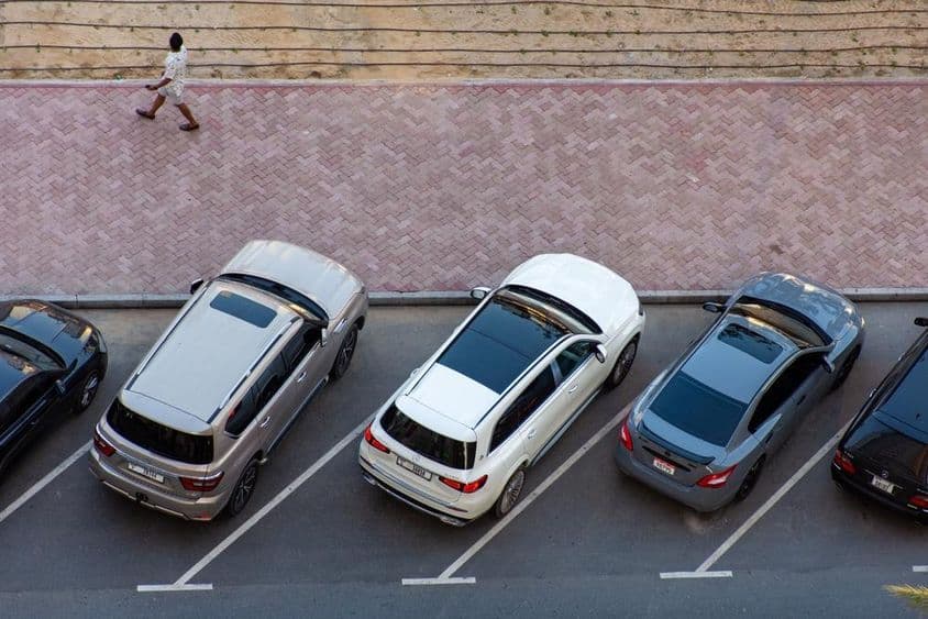 Vista aérea de autos estacionados en Dubai y un hombre caminando en una acera pavimentada.