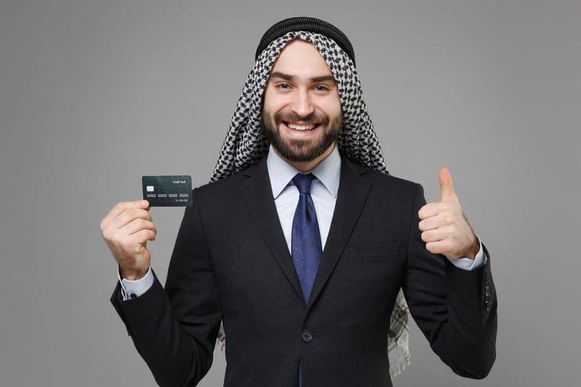 Hombre de negocios árabe musulmán sonriendo con una tarjeta de crédito.