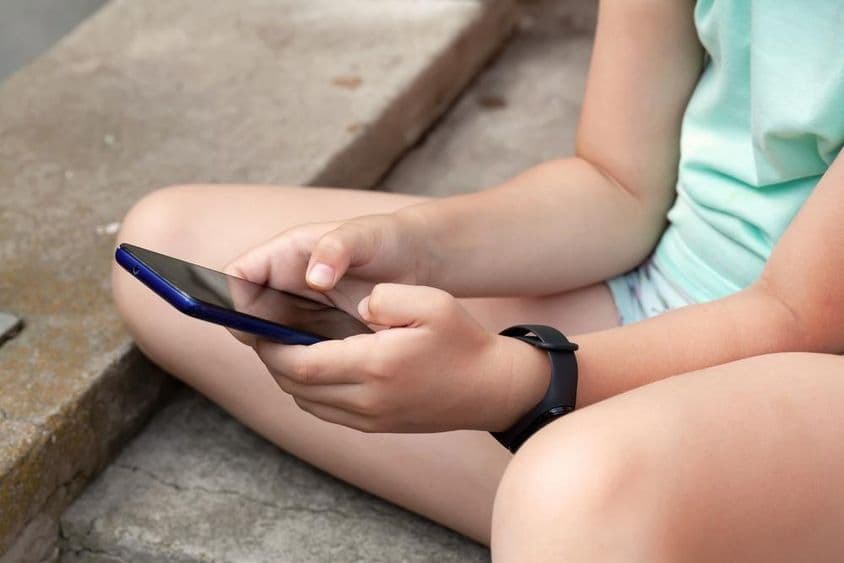 Un niño está sentado al aire libre usando un teléfono inteligente.