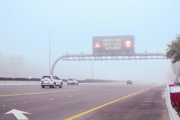 Carretera con niebla y un cartel que menciona Mantén Distancia.