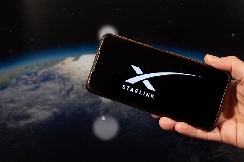 Una mano masculina sosteniendo un teléfono inteligente con el logo de Starlink en su mano derecha.