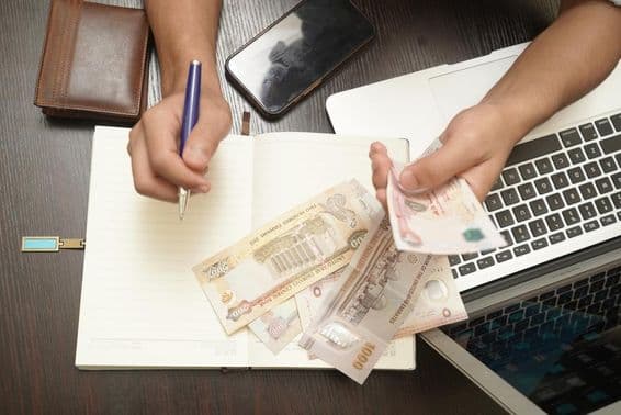 Un hombre contando un fajo de billetes de dirhams de Emiratos Árabes Unidos.