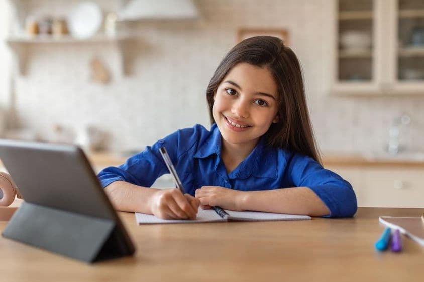 Niña escolar feliz asistiendo a clases desde casa usando una tableta.