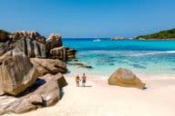 Dos viajeros caminando sobre las suaves arenas blancas de la playa Anse Cocos en Seychelles.