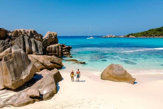 Dos viajeros caminando sobre las suaves arenas blancas de la playa Anse Cocos en Seychelles.