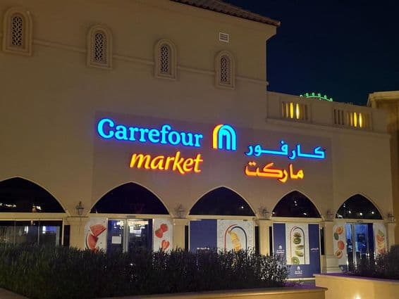 Logotipo iluminado del mercado Carrefour con nombre de marca en árabe