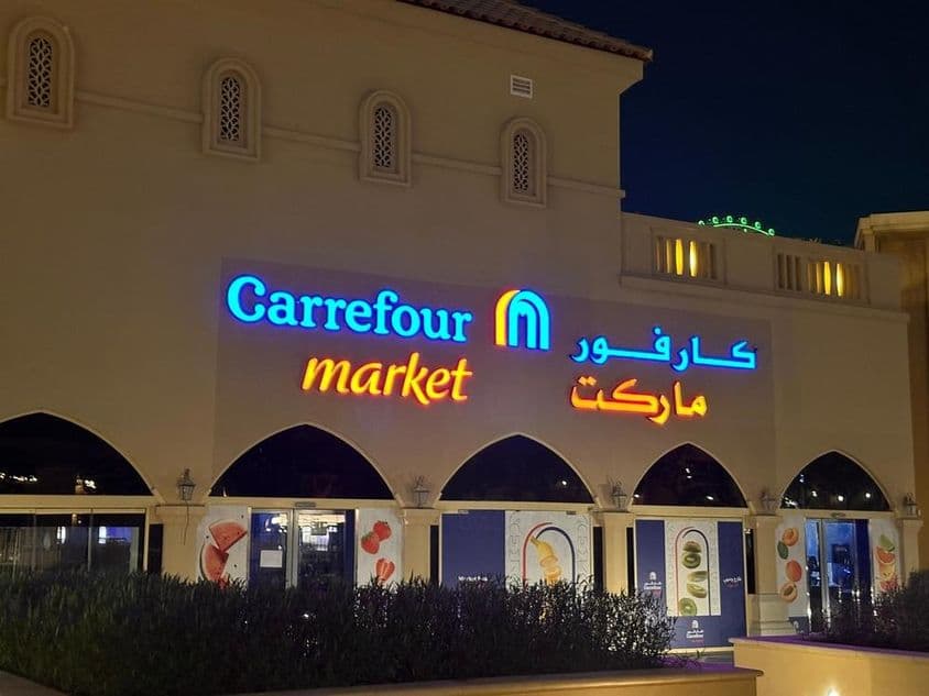Logotipo iluminado del mercado Carrefour con nombre de marca en árabe