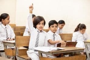 Niño escolar indio feliz levantando la mano