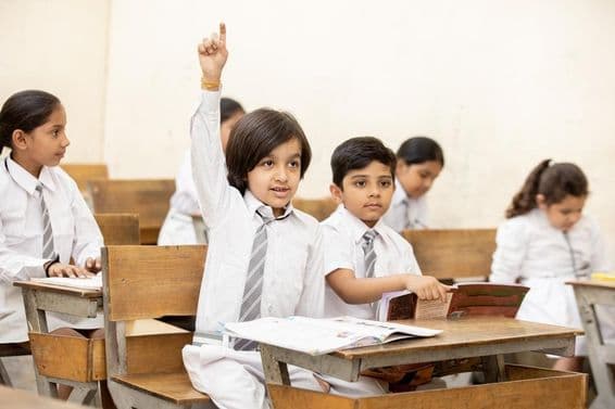 Niño escolar indio feliz levantando la mano