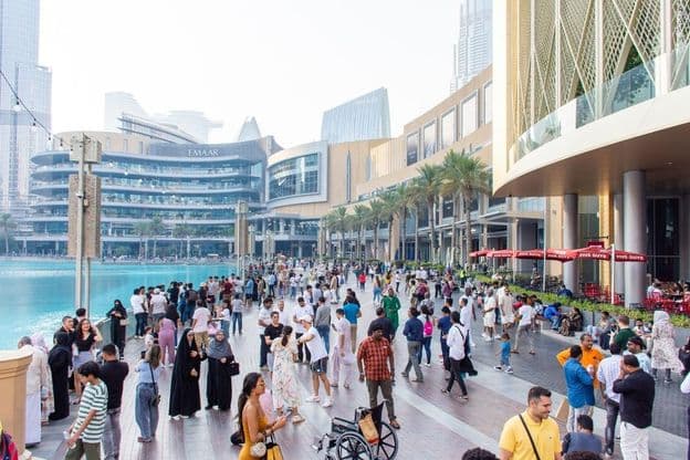 Una multitud diversa de turistas y locales camina por el concurrido paseo marítimo frente al Dubai Mall.